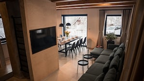 A modern living room with a large sectional sofa, a dining area with a table and chairs, and a TV mounted on the wall. - Villa in Jeseniky With Sauna & Mountain Views (Bela pod Pradedem)