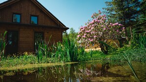 A wooden house with a pond in front, surrounded by greenery and pink flowers. - Villa in Jeseniky With Sauna & Mountain Views (Bela pod Pradedem)