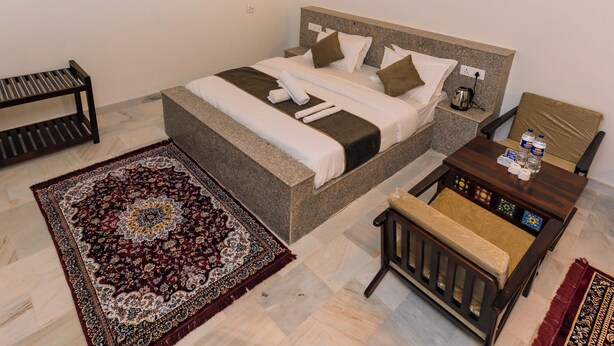 A neatly arranged bedroom with a bed, bedside table, chair, and a decorative rug. - Marubhumi Luxury Resort (Jaisalmer)