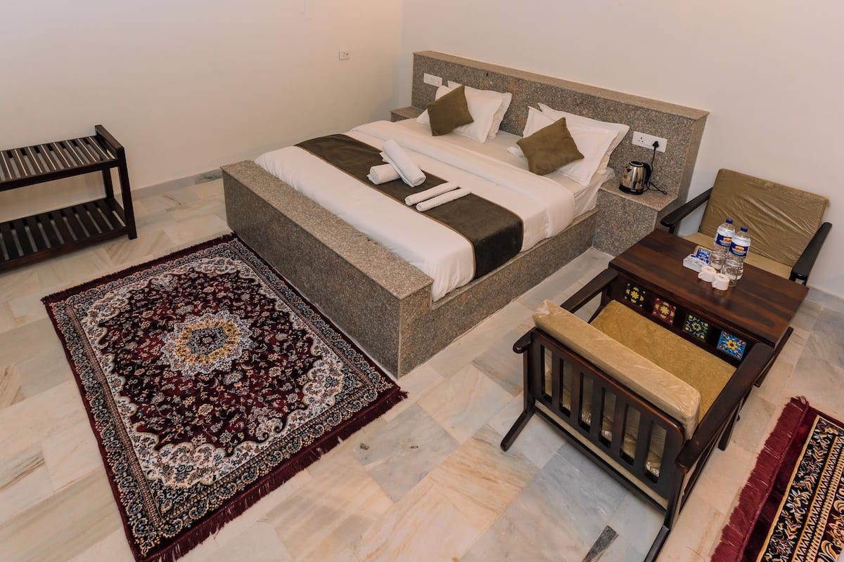 Un dormitorio ordenado con cama, mesita de noche, silla y una alfombra decorativa.