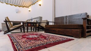 Una habitación con sofá de madera, un tapete estampado, una mesita con una botella de agua y un ventilador de pared.