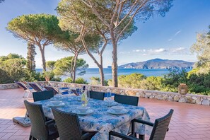 An outdoor dining area with a table set for six, overlooking a scenic view of the sea and mountains. - Villa with private access to the beach (Capoliveri)