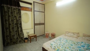 A bedroom with a bed, a wardrobe, a small table, and a trash bin. - Om Trance Homestay (Jaipur)