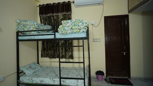 A bunk bed room with a curtain, an air conditioner, a door, and a trash bin. - Om Trance Homestay (Jaipur)