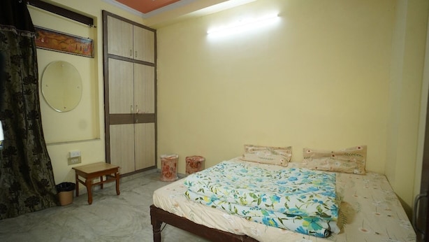 A bedroom with a bed, a wardrobe, a mirror, a small table, and a trash bin. - Om Trance Homestay (Jaipur)