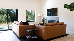 Una sala de estar moderna con un sofá de cuero marrón, una mesa de centro de vidrio y un televisor de pantalla plana montado en la pared.
