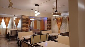 Un'area pranzo moderna con diversi tavoli e sedie, ventilatori a soffitto e luci a sospensione.