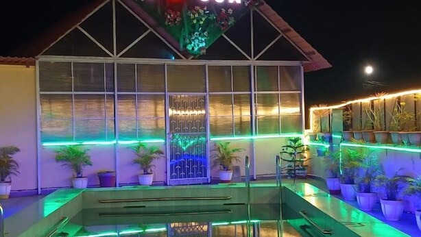 Un edificio con un cartello che recita 'I ♥ GOA' e un'area piscina con piante in vaso e illuminazione verde.