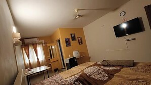Una camera da letto con un letto, una scrivania, una sedia, un televisore e una finestra con tende.