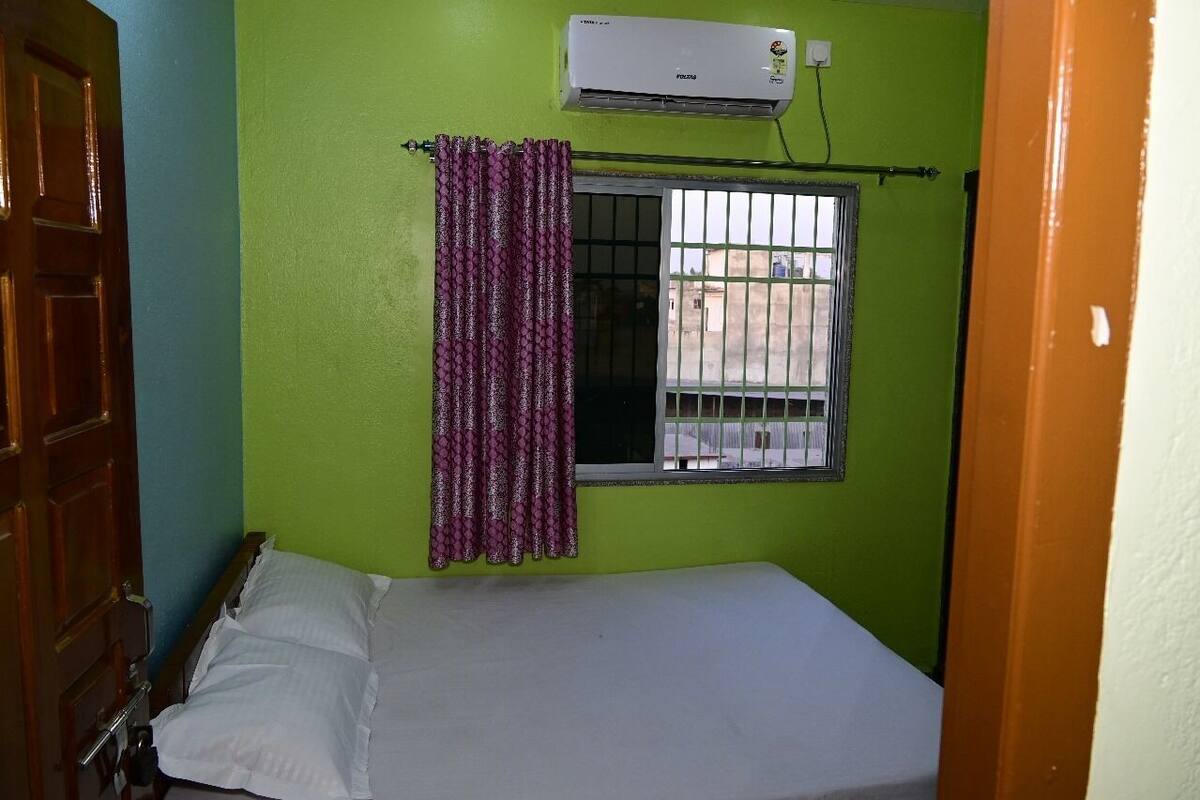 A small room with a single bed, a window with bars, and an air conditioning unit on the wall.