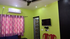Une pièce avec un lit, un ventilateur de plafond, un climatiseur, une télévision et deux chaises rouges.