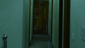 Un couloir étroit, avec une porte en bois au fond, des spots encastrés et un luminaire au plafond.