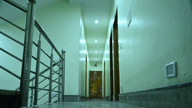 Un couloir avec une rambarde en métal, une porte en bois au fond et un luminaire au plafond.
