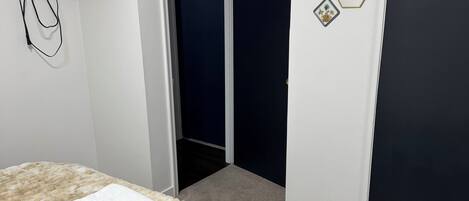 Une chambre à coucher avec un lit, un mur blanc, une porte sombre et un couloir menant à une autre pièce.