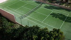 An outdoor tennis court surrounded by greenery and a stone wall.