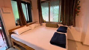 A single bed with white linens, two pillows, and a decorative pillow. The room has a window with patterned curtains and a view of greenery outside. - RS Farms (Bhiwandi)
