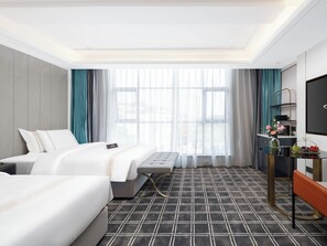 A hotel room with two beds, a large window with curtains, a TV, a small table with a vase of flowers, and a patterned carpet.