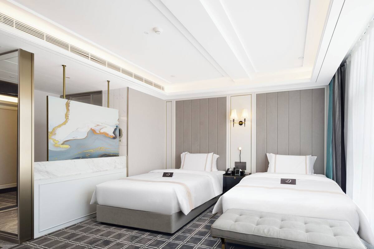 Een hotelkamer met twee bedden, een kleine zithoek, een grote spiegel en een schilderij aan de muur.