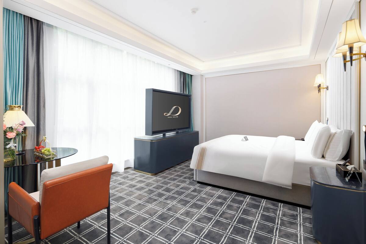 Een hotelkamer met een bed, een televisie op een standaard, een bureau met een lamp en een stoel.