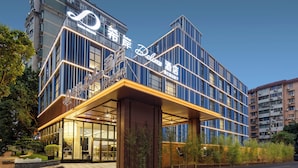 A modern hotel with a prominent sign, large windows, and a well-lit entrance. - Pazhou XANA Deluxe International Hotel Pazhou Convention and Exhibition Center Nanzhou Subway Metro Branch - Free Shuttle Bus to Canton Fair Complex During Canton Fair Period (Guangzhou)