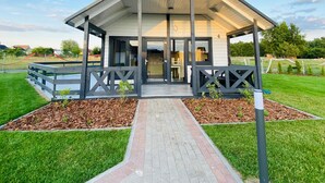 A modern pavilion with a covered entrance, a brick pathway leading to it, and a grassy lawn. - Summer House in Jaroslawiec Near Beach (Postomino)
