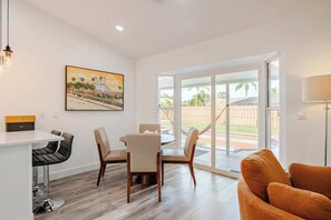 A modern living room with a dining area, a large window, and a painting on the wall.