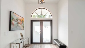 Un pasillo con puerta de vidrio, un banco, una consola con una escultura y un cuadro en la pared.