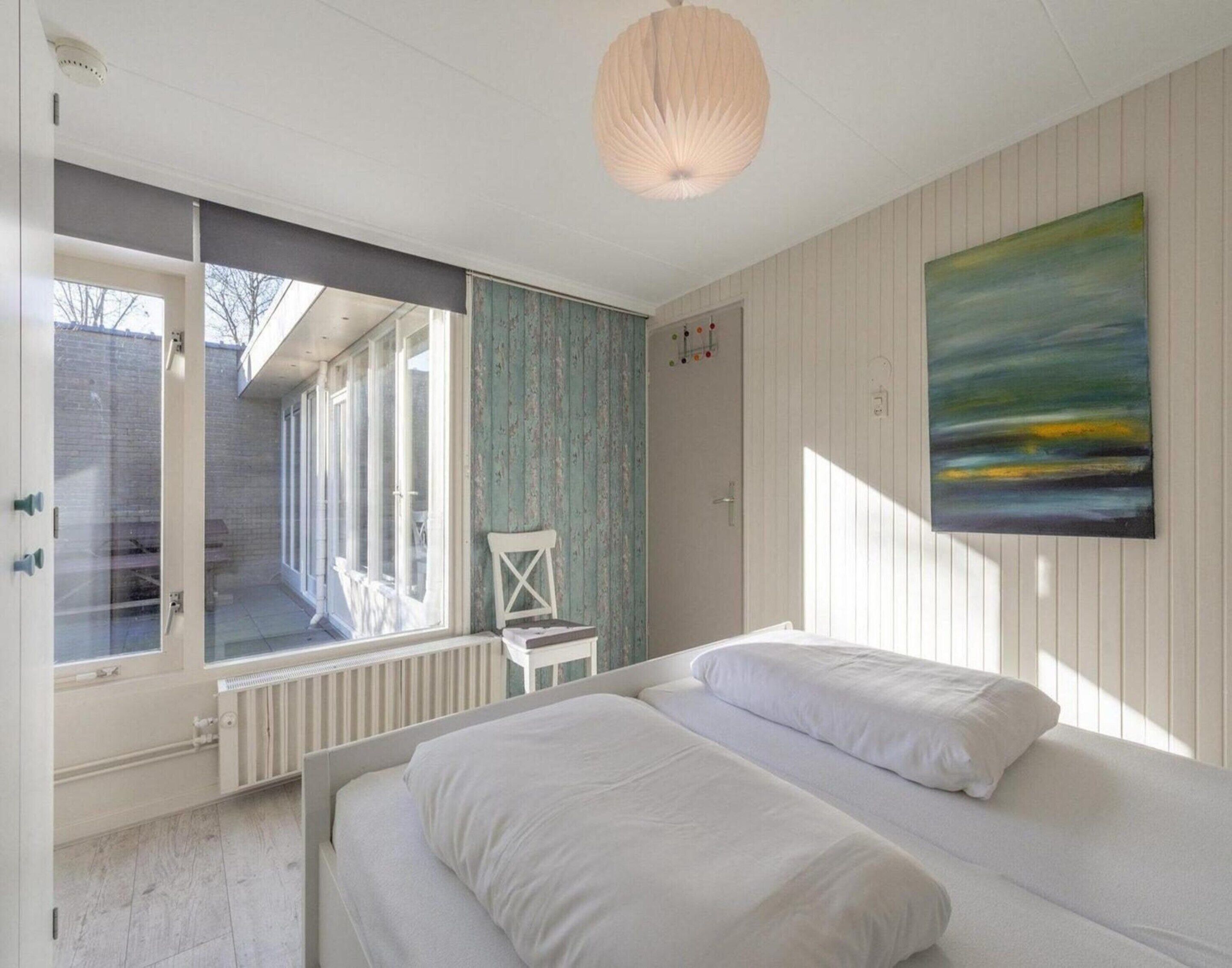 Una camera da letto con un letto, una sedia, una finestra e un quadro appeso al muro.