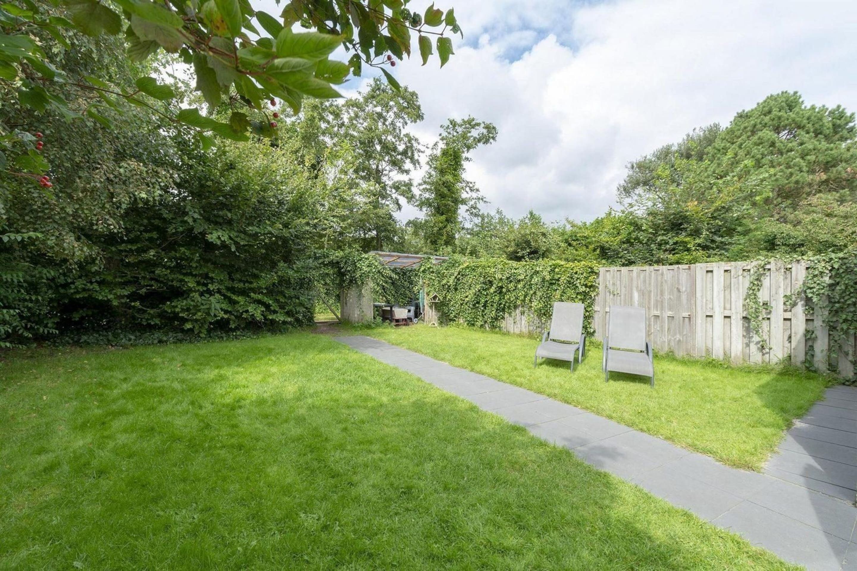A backyard with a paved path, a wooden fence, and a bench.