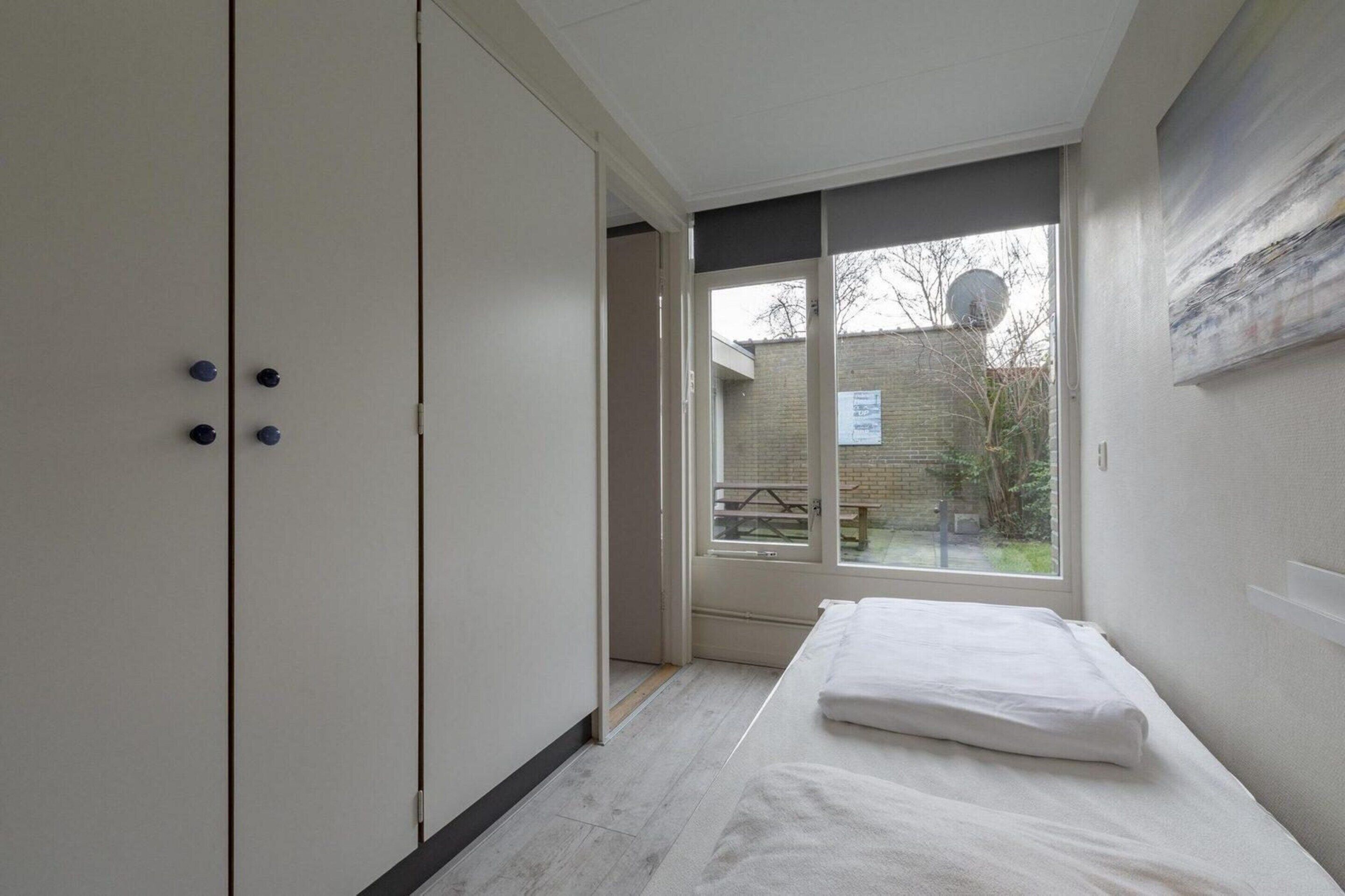 A bedroom with a bed, a wardrobe, and a view of the outside.