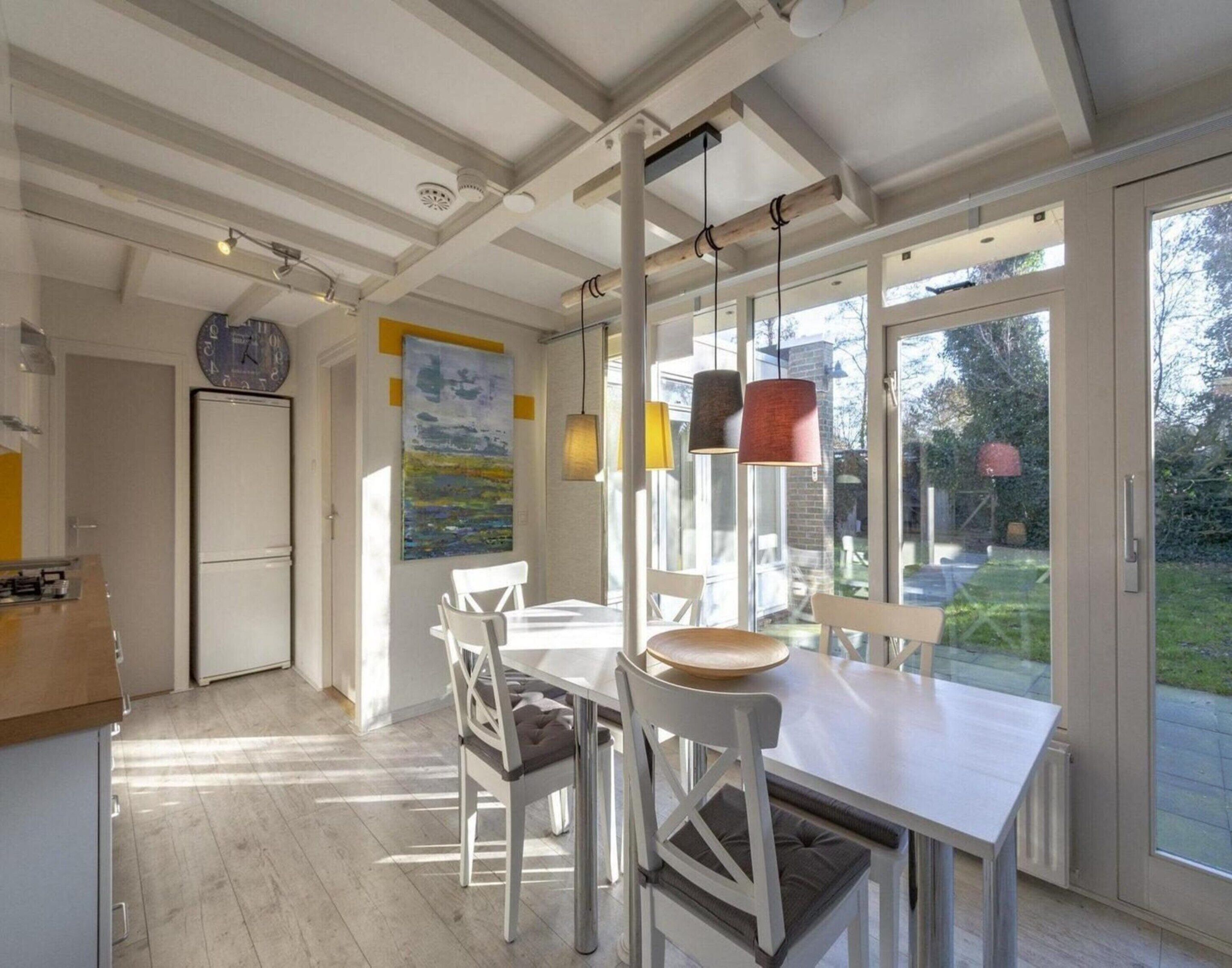 A modern kitchen with a dining area, large windows, and a view of the outdoors.