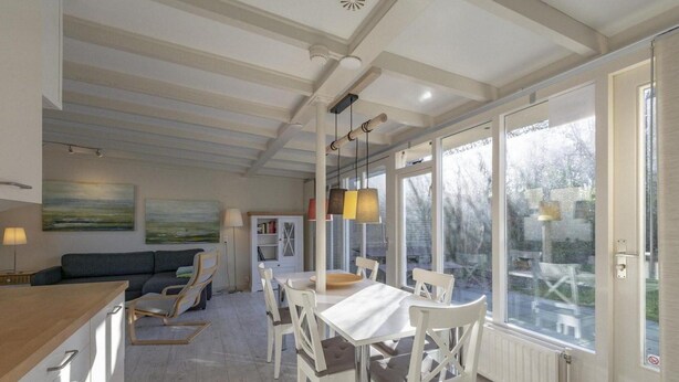 Een moderne keuken met witte kasten, een eethoek met witte stoelen en een tafel, en grote ramen met uitzicht op de omgeving.