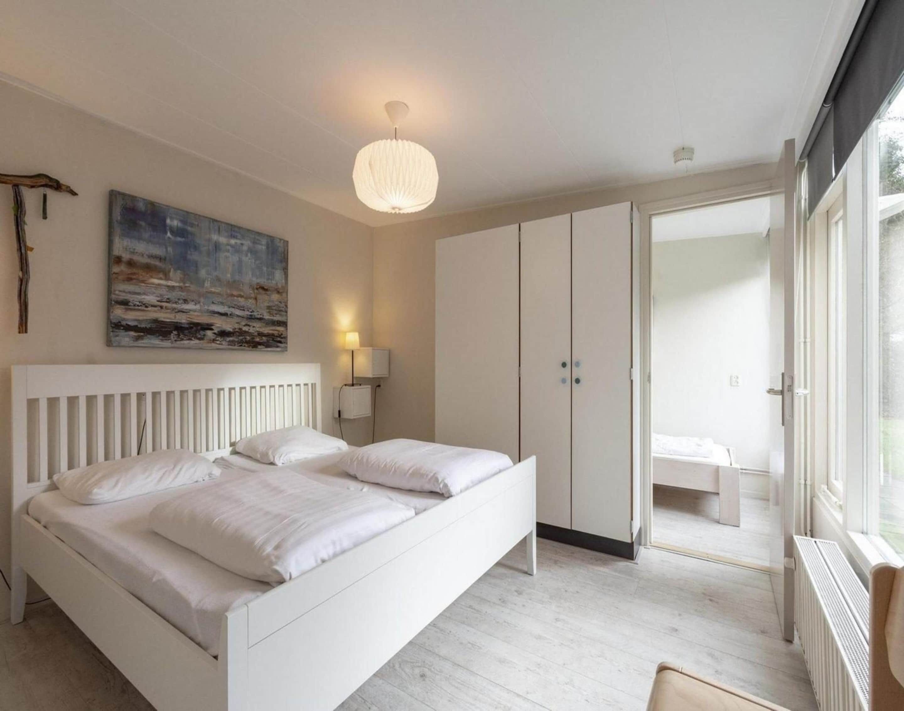 A bedroom with a bed, a painting, a lamp, and a wardrobe.