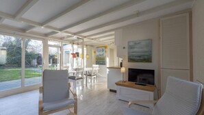 Een moderne woonkamer met een open haard, grote ramen en een eethoek.