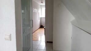 Un couloir avec une porte en verre donnant sur une pièce, un sol carrelé et un ventilateur de plafond.