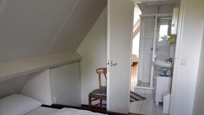 Une chambre à coucher comprenant un lit, une chaise et donnant sur une salle de bain avec un lavabo et des toilettes.