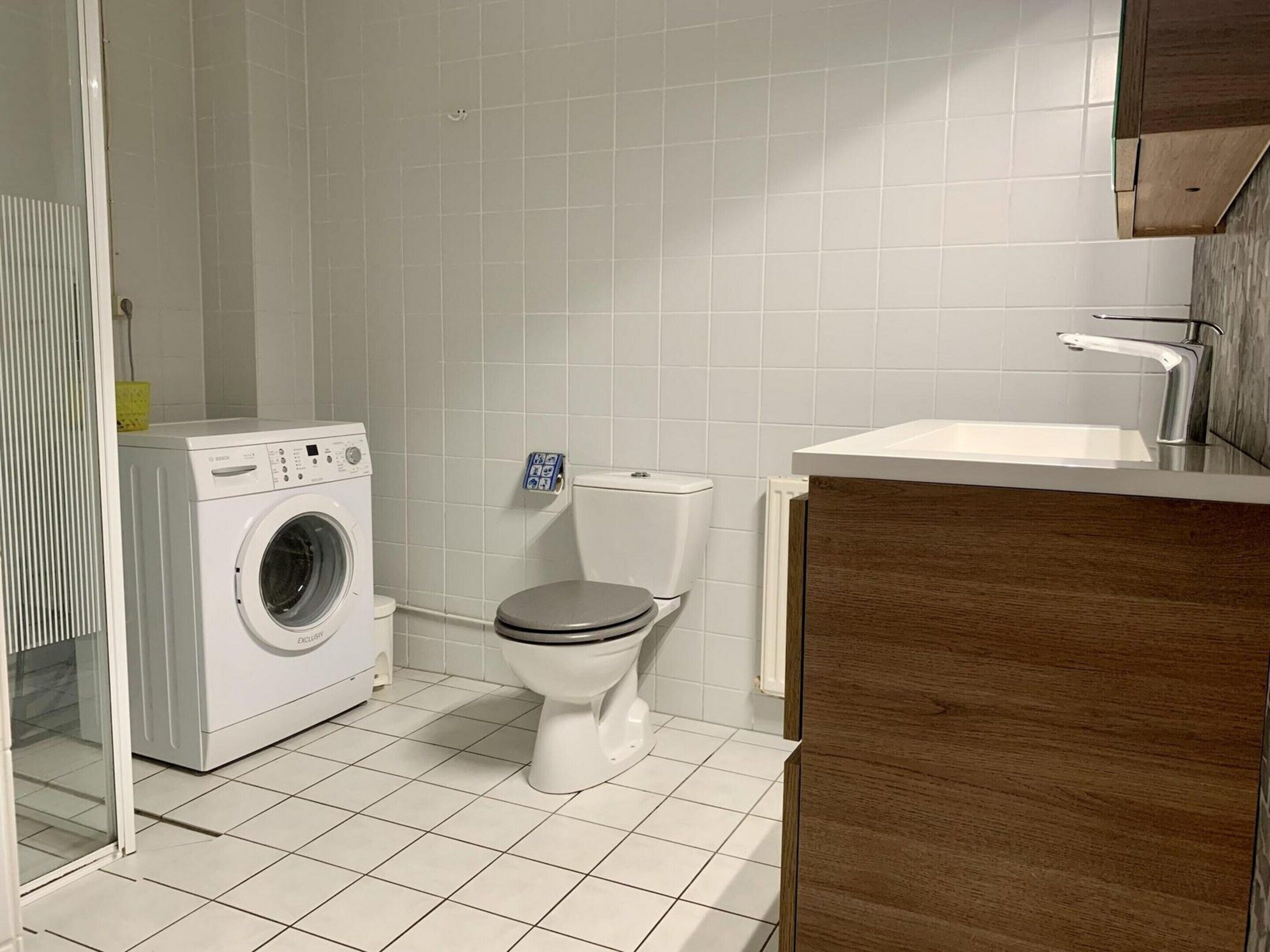 A bathroom with a washing machine, toilet, and wooden vanity with a sink.
