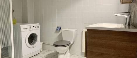 A bathroom with a washing machine, toilet, and wooden vanity with a sink.
