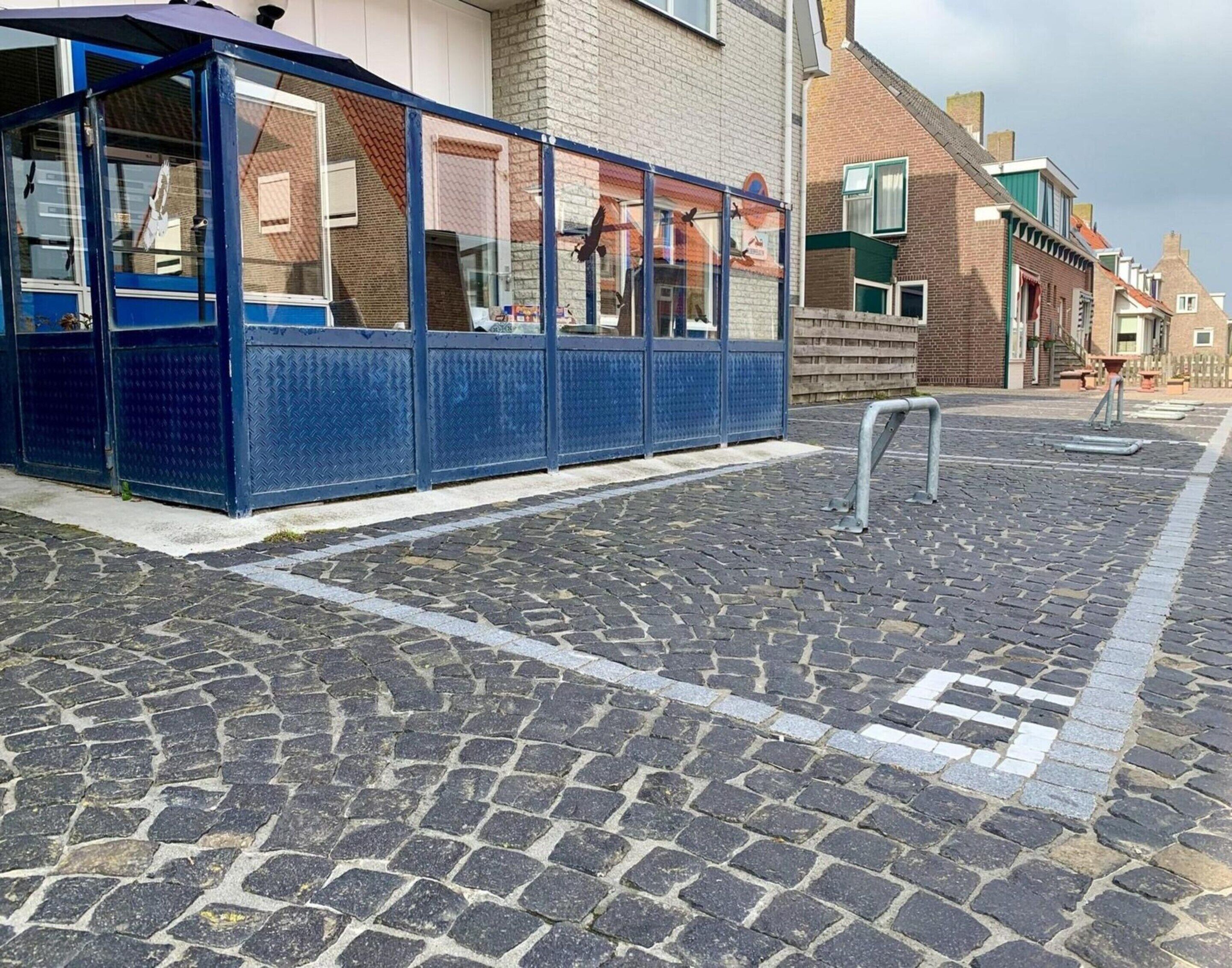 Un área de estar al aire libre con cubierta azul y barandilla de metal, junto a un edificio de ladrillo con ventana y puerta.