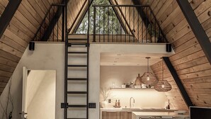 Une pièce de style « loft », avec un plafond en bois, un coin cuisine, un escalier et un espace salon comprenant un canapé et un fauteuil.