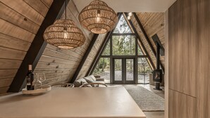 Une cuisine moderne dotée d’un grand îlot central, de poutres en bois et de grandes fenêtres offrant une vue sur la forêt.