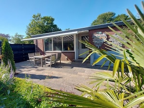 A patio area with a table and chairs, a covered seating area, and a brick wall with a decorative mural. - Holiday Retreat in Sint Maartenszee (Sint Maartensvlotbrug)