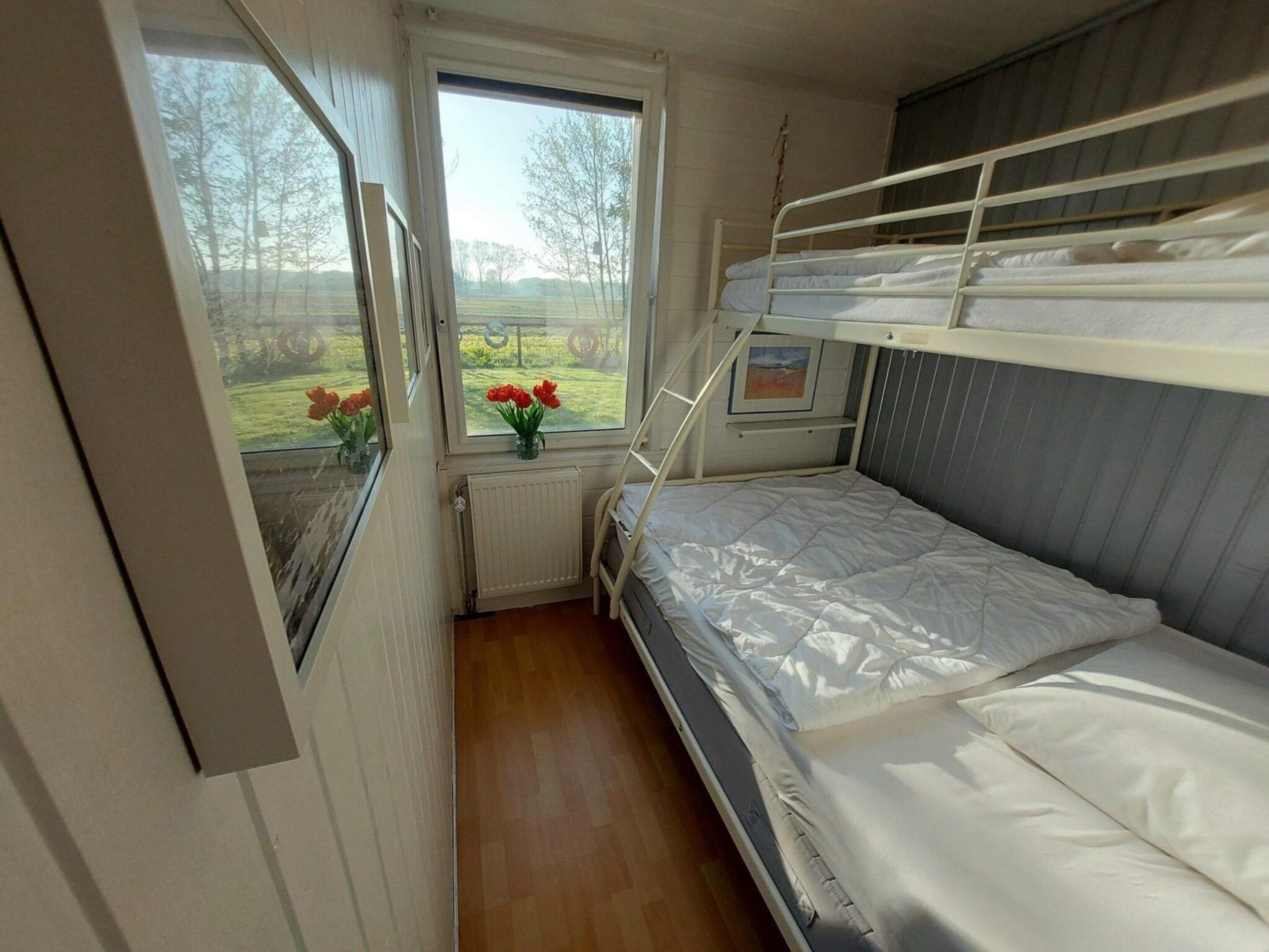 Une chambre avec un lit superposé, une fenêtre, un radiateur et un tableau encadré au mur.