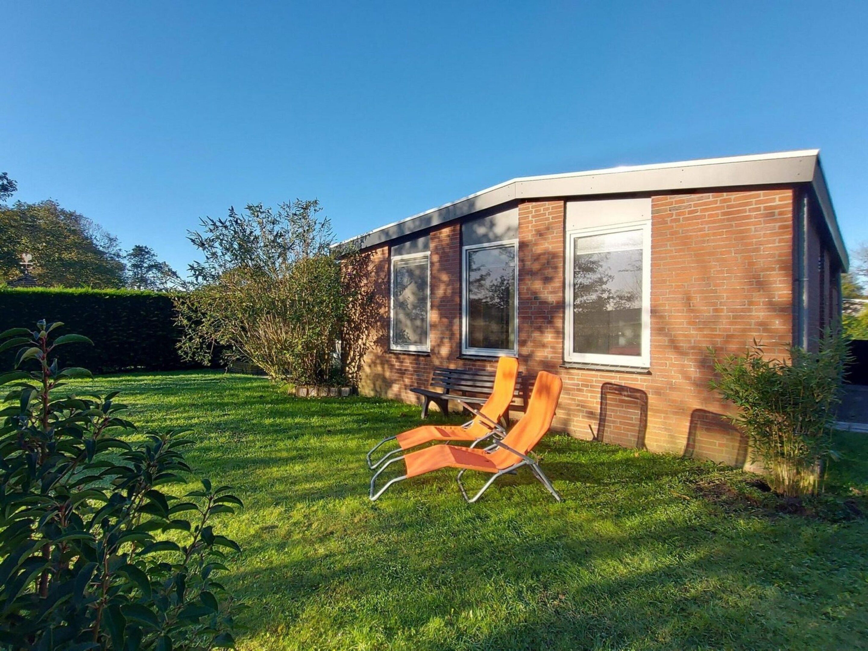 A modern house with a brick exterior, large windows, and a well-maintained lawn with outdoor furniture.