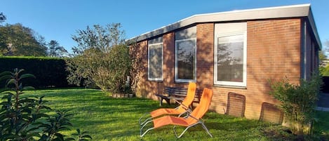 A modern house with a brick exterior, large windows, and a well-maintained lawn with outdoor furniture.