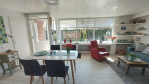 Ein modernes Wohnzimmer mit Essbereich, einem roten Sessel und einer durch eine Glastür sichtbaren Küche.