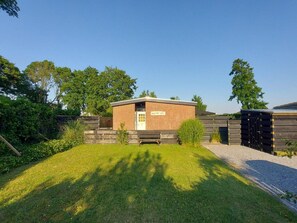 A small brick building with a door and windows, surrounded by a wooden fence and greenery. - Holiday Retreat in Sint Maartenszee (Sint Maartensvlotbrug)