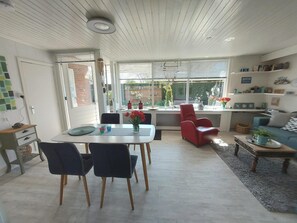 Un espace de vie moderne comprenant un coin repas, un fauteuil rouge, un canapé et un coin cuisine donnant sur le jardin.