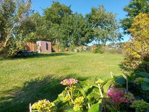 Un jardin bien entretenu, avec une petite construction en briques, une clôture en bois et diverses plantes.