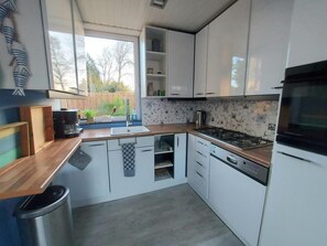 A modern kitchen with white cabinets, a wooden countertop, a gas stove, and a stainless steel sink. - Holiday Retreat in Sint Maartenszee (Sint Maartensvlotbrug)
